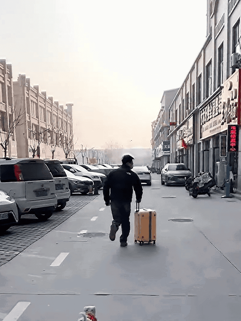 Person walking in city with rolling suitcase and pet carrier.