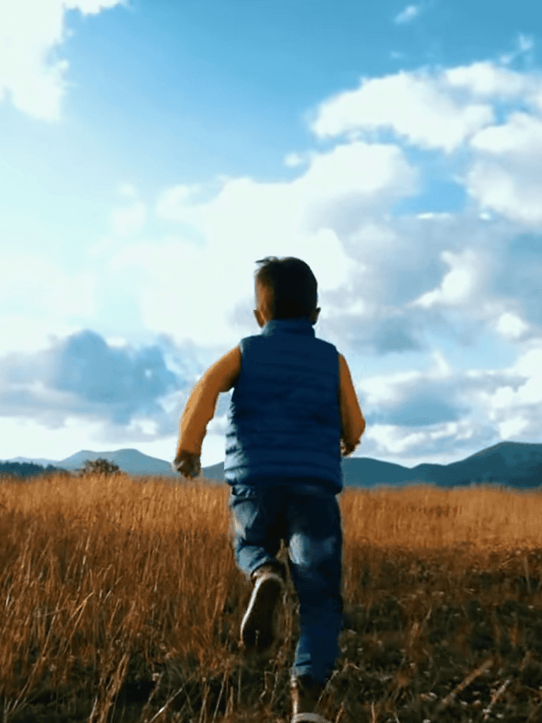 Child running in open field during daytime, enjoying outdoor adventure.
