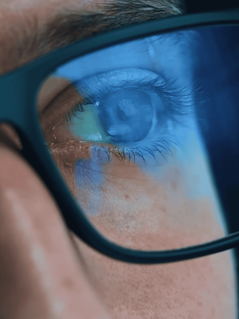Close-up of a person's eye with glasses reflecting digital screen.