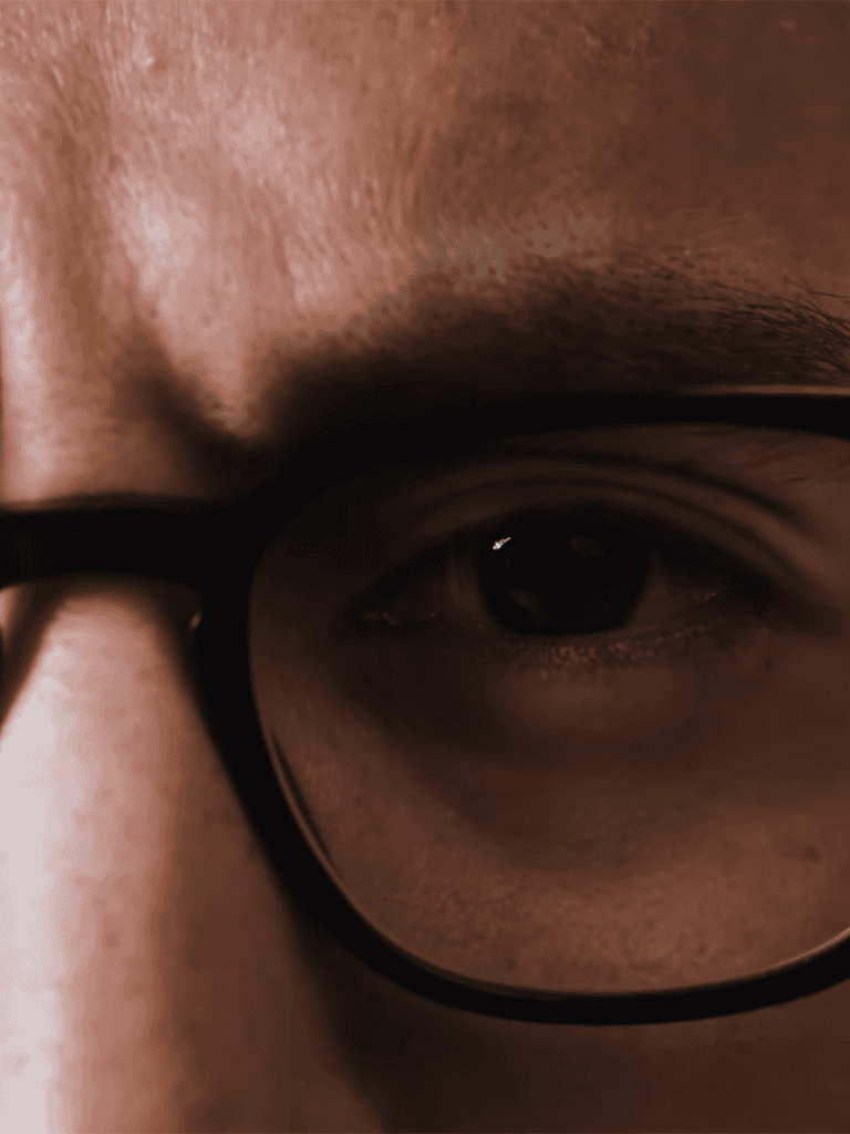 Close-up photo of a person's eye behind black glasses, highlighting facial features.