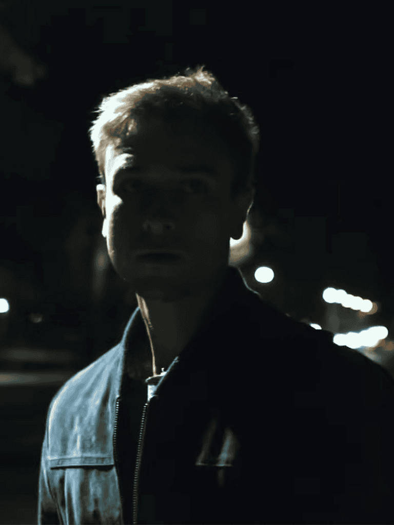 Young man in dark night scene portrait, streetlights in background, mysterious mood.