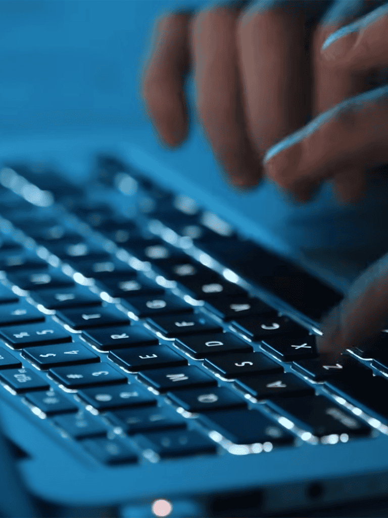 Close-up of hands typing on a blue illuminated keyboard in a dark environment.