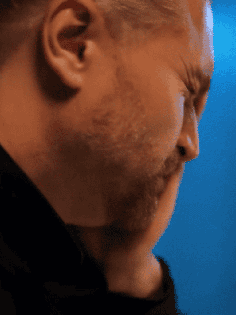 Close-up of stressed man with hand on face, showing frustration and concern.