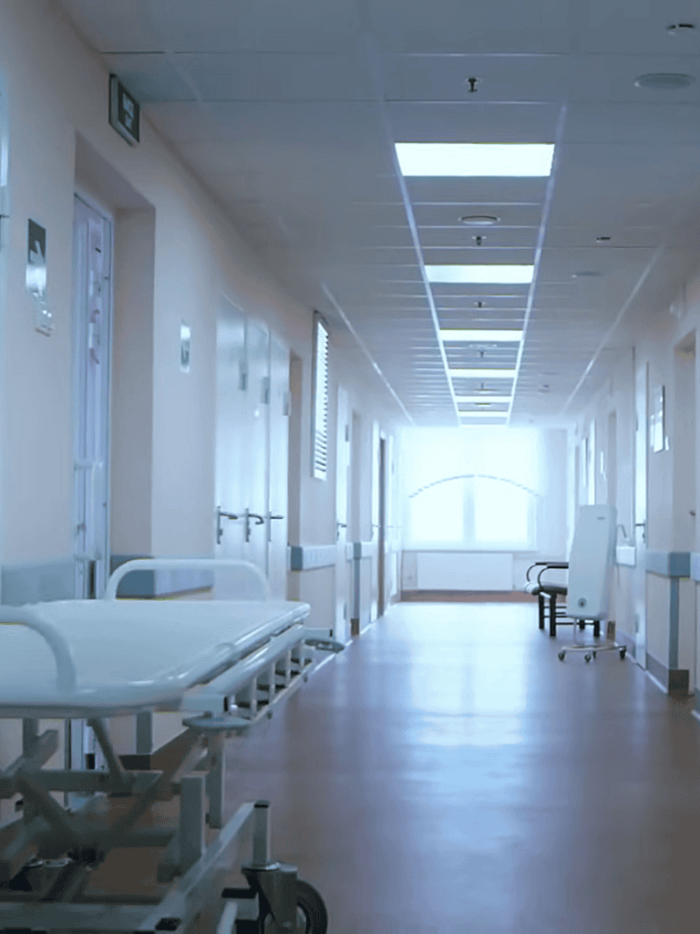 Bright hospital hallway with empty patient beds and chairs, modern medical facility, healthcare environment, sanitized clinical space.