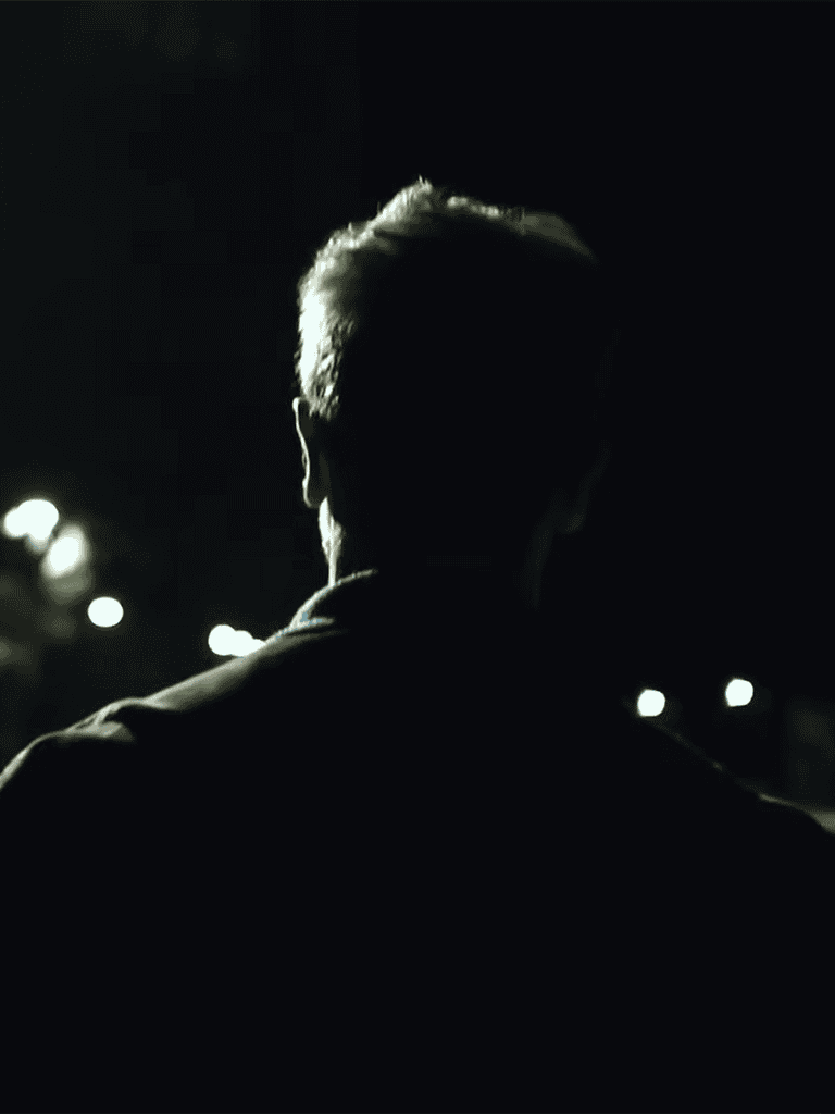Dark person silhouette at night with blurred streetlights background.