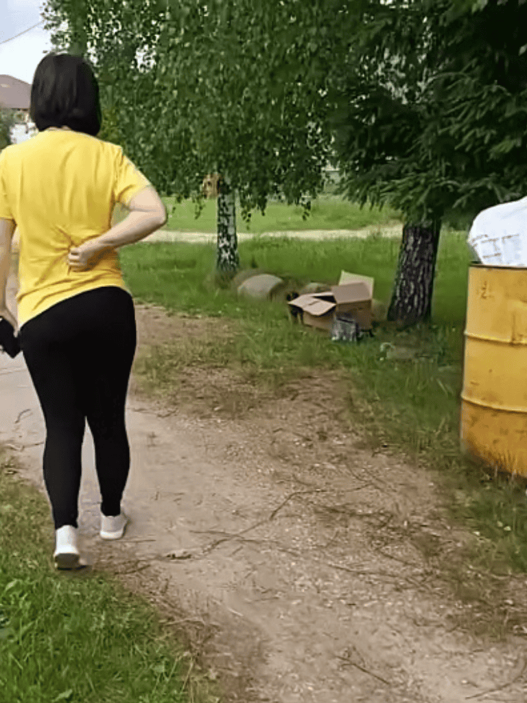 Woman walking with a dog on nature trail, surrounded by trees and greenery.