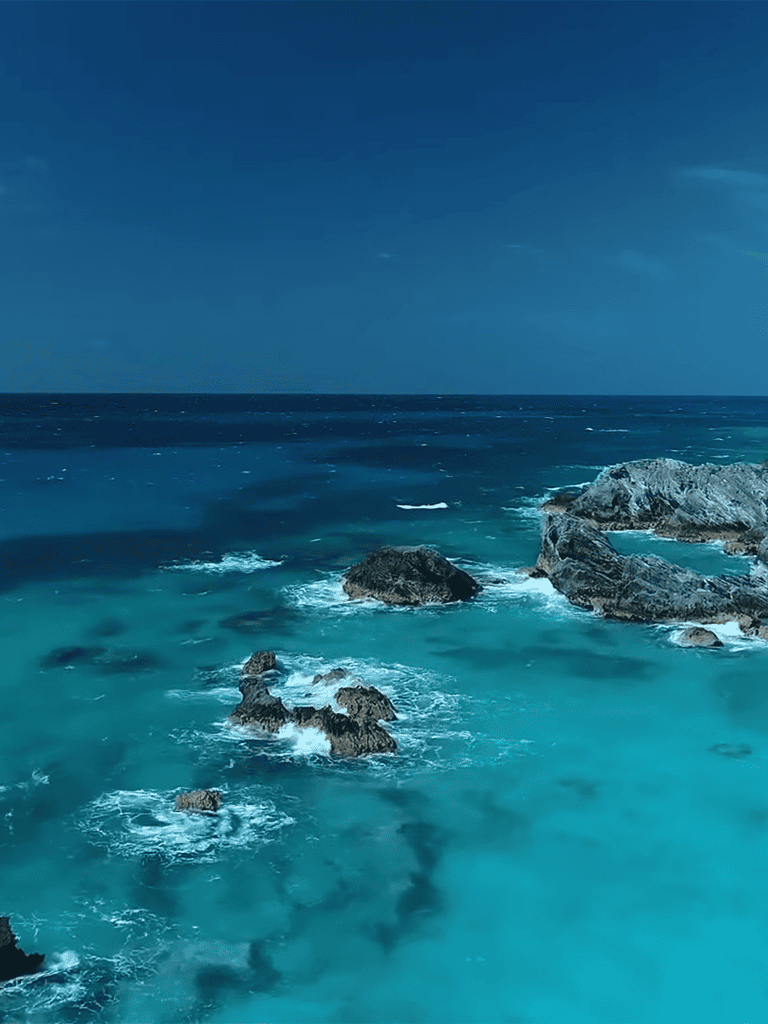 Beautiful ocean scene with rocky coastline and clear blue waters under a bright sky.