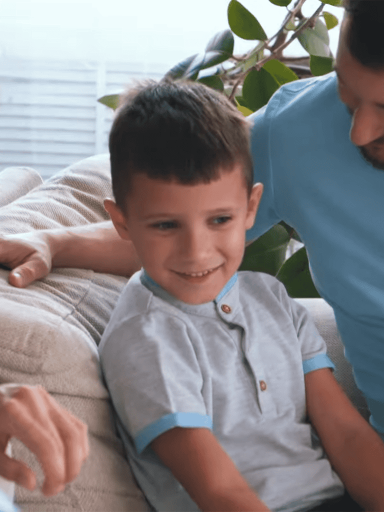 Smiling boy sitting on couch with dad, family bonding, happy moments, indoor leisure.