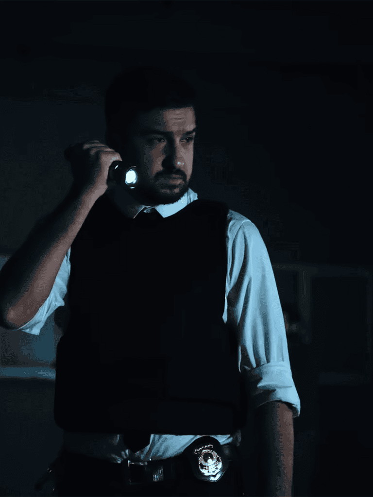 Detective wearing a vest, holding a flashlight, investigating in a dark setting.