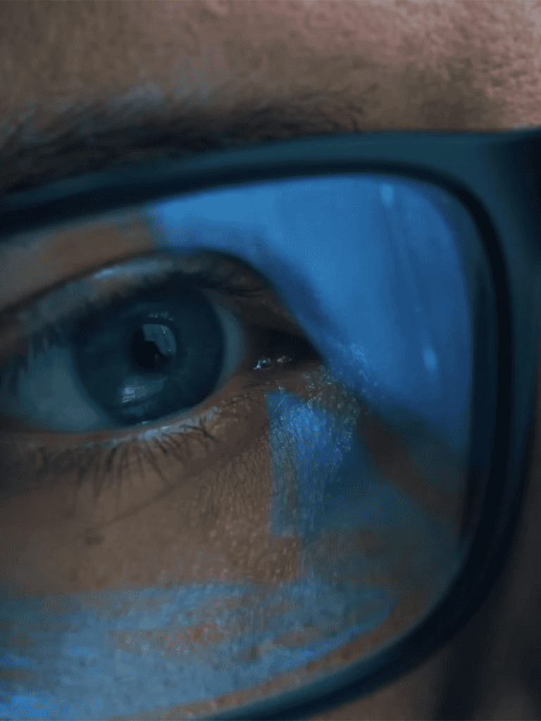 Close-up of a person wearing glasses with reflection of a computer screen in the lenses.