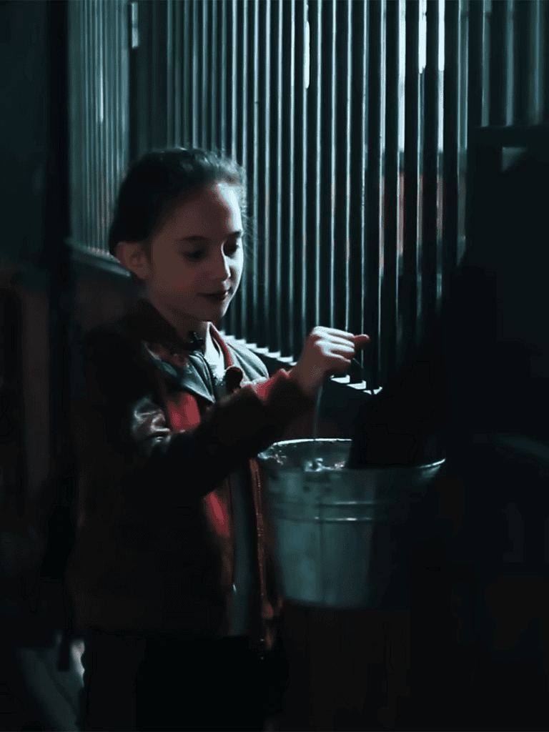 Young girl placing food in a bucket for a dog at a shelter.