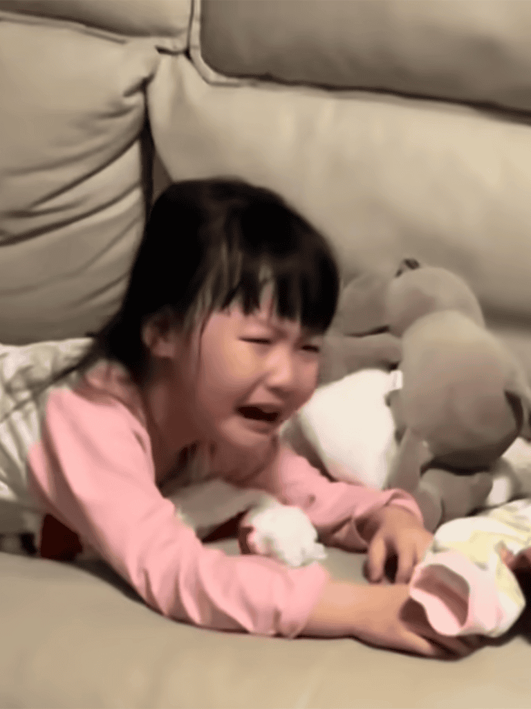 Girl crying and upset on sofa with plush toys, emotional moment captured.